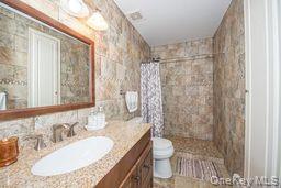 63 East Tiana Road Hampton Bays, NY 11946 - Photo 22 of 30 a bathroom with a granite countertop sink a toilet a mirror and shower
