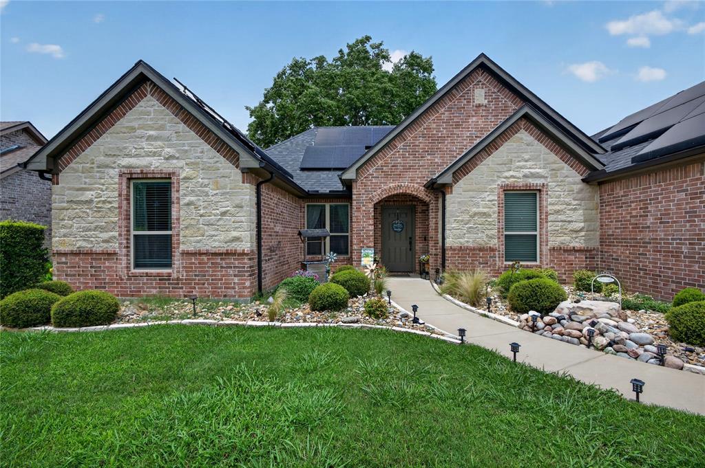 701 West Lamberth Road Sherman, TX 75092 - Photo 4 of 37 Brick and stone facade residence featuring a covered entry, integrated solar panels, a concrete pathway with landscape lighting, and a rock garden with mature shrubs