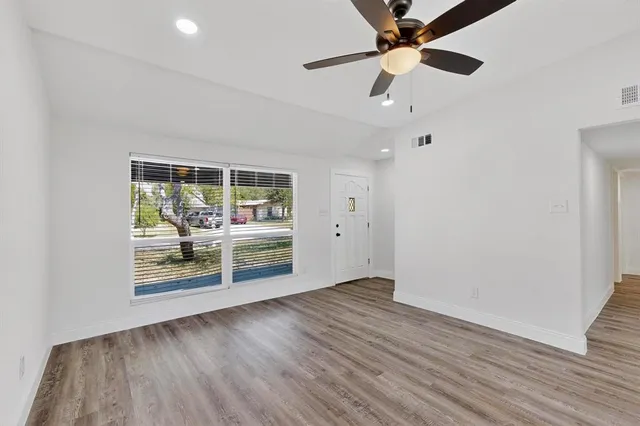 an empty room with wooden floor chandelier fan and windows