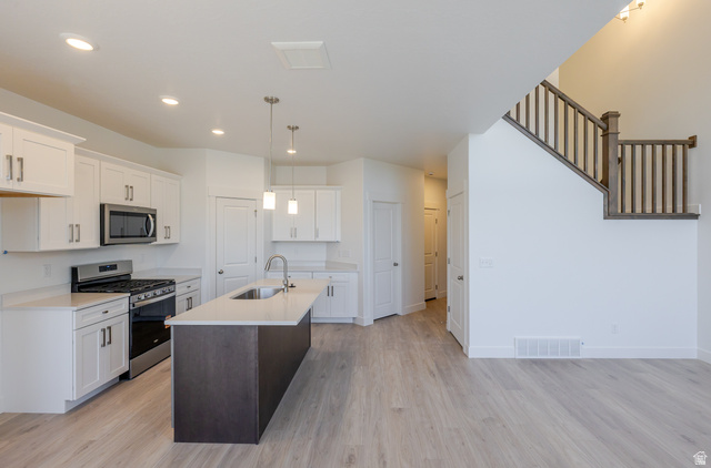 4720 Heartwood Road, Unit 438 Mapleton, UT 84664 - Photo 4 of 19 Dual tone kitchen with stainless steel appliances, a kitchen island with sink, light stone countertops, light wood finished floors, and two tone cabinets