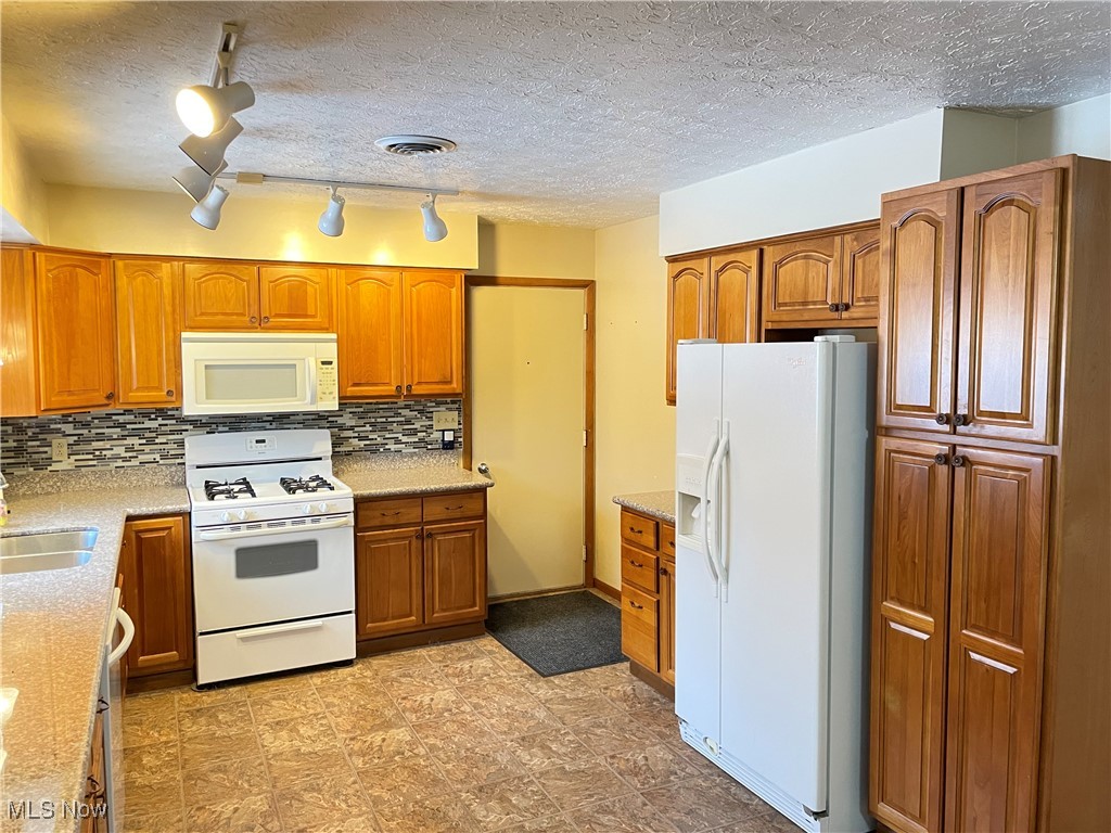 1381 Robb Road Conneaut, OH 44030 - Photo 17 of 50 Kitchen featuring white appliances, brown cabinets, a textured ceiling, backsplash, and light stone countertops