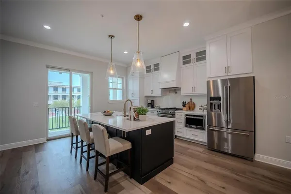 a kitchen with granite countertop a refrigerator a stove a dining table and chairs with wooden floor