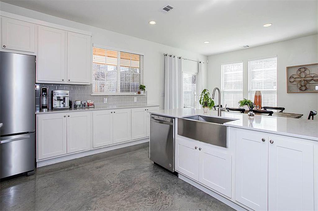 1311 Fort Branch Boulevard Austin, TX 78721 - Photo 11 of 27 Kitchen featuring concrete floors, a sink, decorative backsplash, stainless steel appliances, and white cabinetry