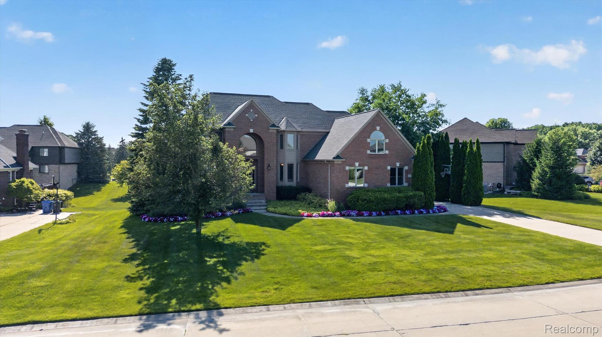 3804 Elk Drive Rochester, MI 48306 - Photo 59 of 75 Brick exterior residence featuring a symmetrical facade, arched entry, multiple gabled rooflines, a concrete driveway, and mature landscaping with manicured lawns and flowering beds