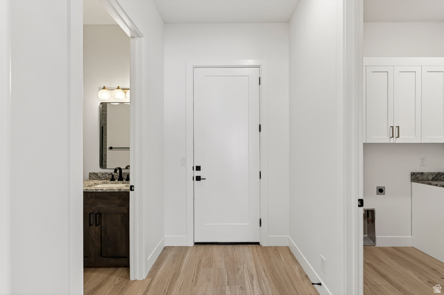 2862 South Mountain Rnch Road Cedar City, UT 84720 - Photo 20 of 64 Hallway with wood-finish flooring, featuring a solid core door with matte black hardware, and views into a vanity area with a granite countertop and a utility area with white cabinetry