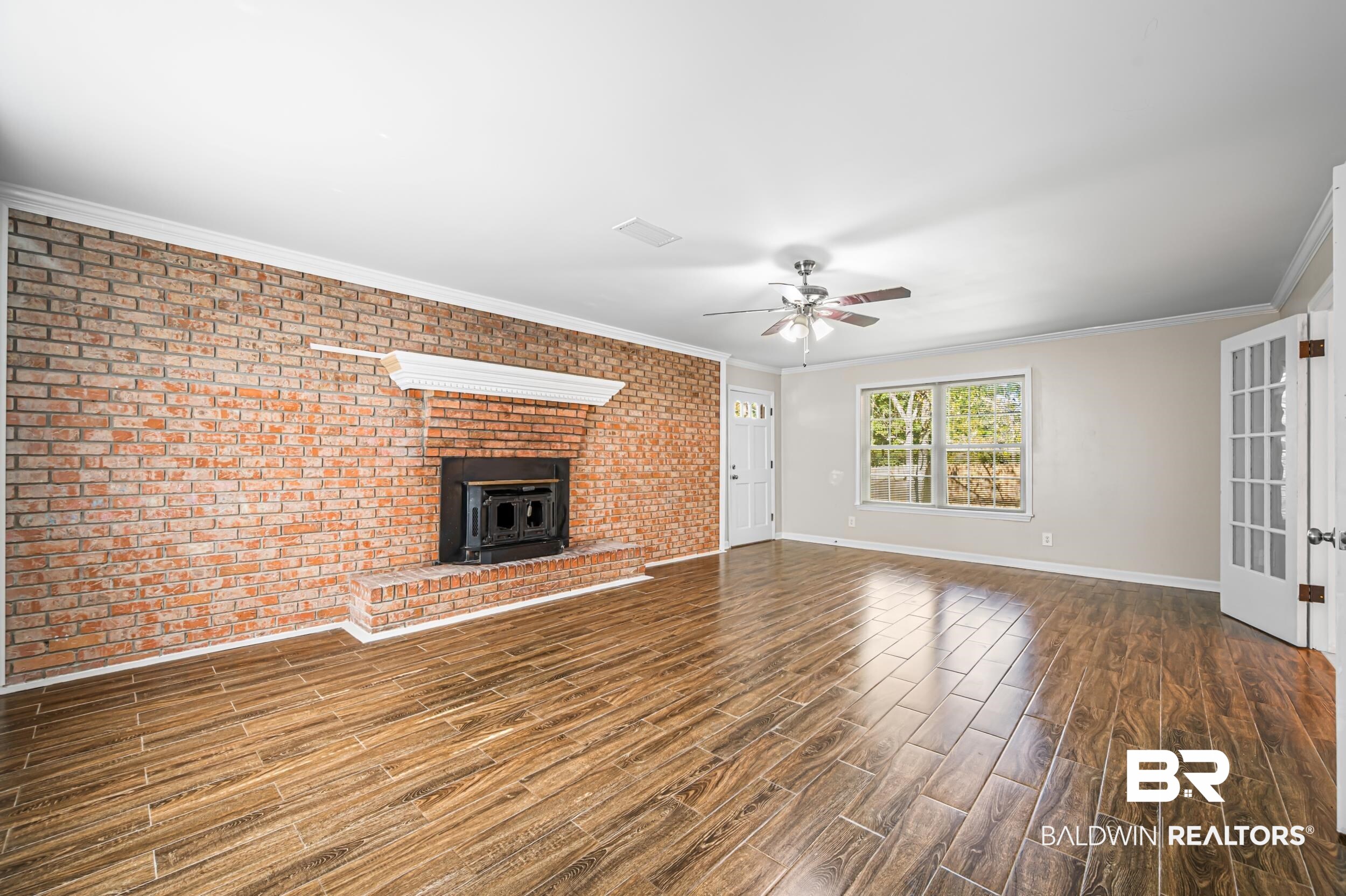 1605 Collier Avenue Bay Minette, AL 36507 - Photo 15 of 36 Unfurnished living room featuring brick wall, a wood stove, dark wood-style flooring, crown molding, and ceiling fan