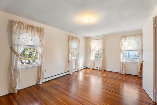 an empty room with wooden floor and windows with curtains view