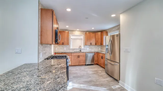 a kitchen with stainless steel appliances granite countertop a stove a sink dishwasher a refrigerator and white cabinets with wooden floor