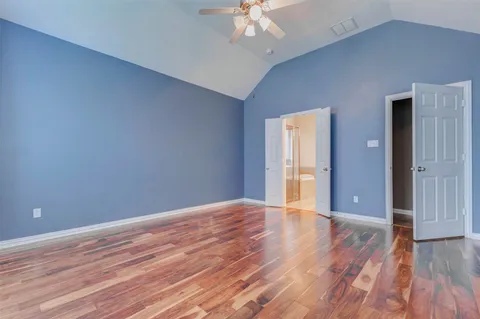 a view of an empty room with wooden floor and a ceiling fan