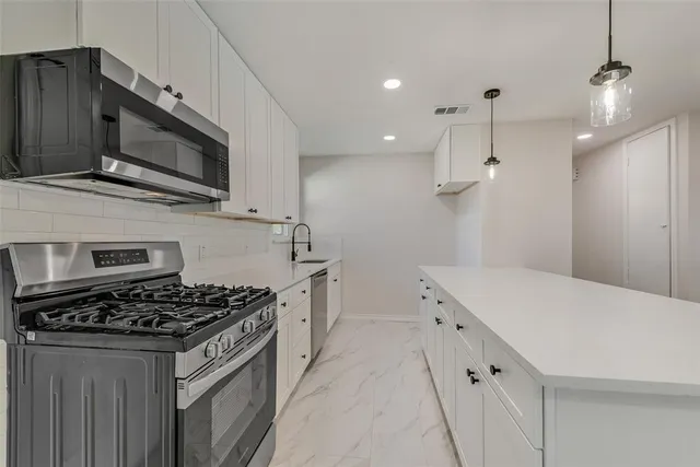 a kitchen with stainless steel appliances a stove a microwave a sink and white cabinets