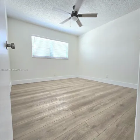 an empty room with wooden floor ceiling fan and windows