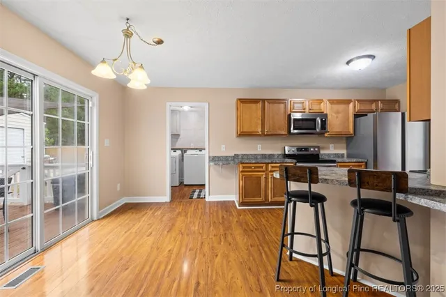 a kitchen with stainless steel appliances a microwave a stove top oven a sink dishwasher a dining table and chairs with wooden floor