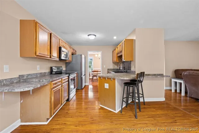 a kitchen with stainless steel appliances granite countertop a stove top oven a sink a dining table and chairs with wooden floor