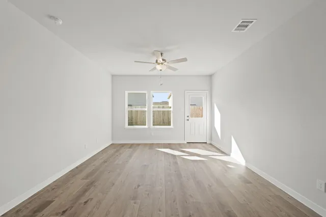 an empty room with wooden floor chandelier fan and windows