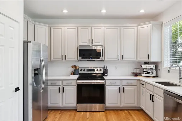 a kitchen with stainless steel appliances granite countertop white cabinets a sink a stove a refrigerator and a microwave