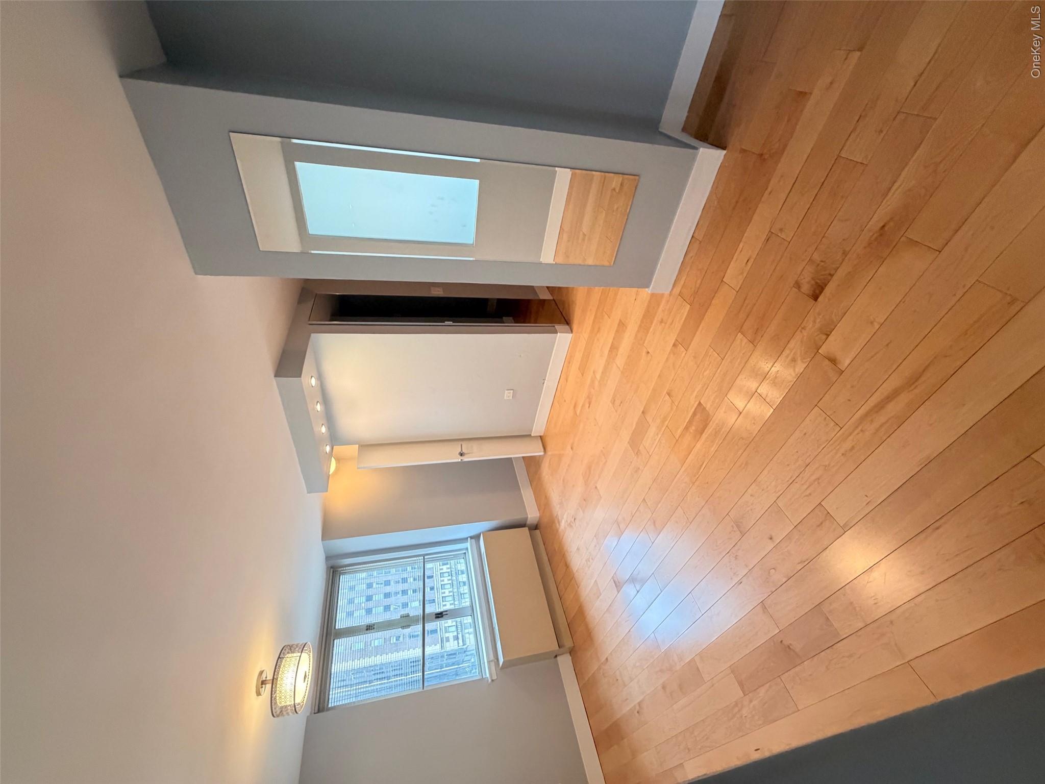 225 Rector Place, Unit 7E Manhattan, NY 10280 - Photo 2 of 19 Hardwood flooring throughout, featuring a window with city buildings visible, a ceiling-mounted light fixture, recessed lighting, and a full-length wall mirror