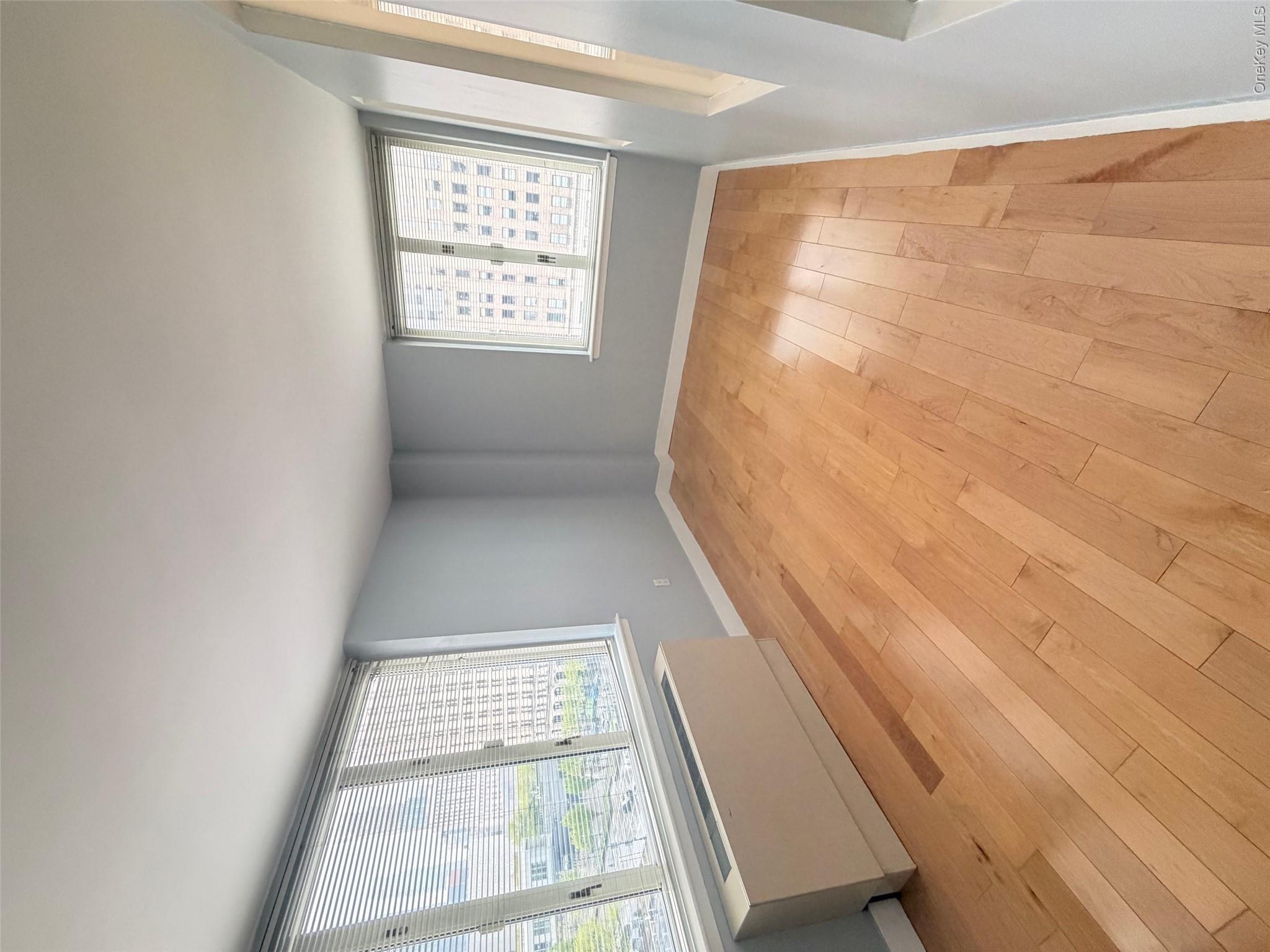 225 Rector Place, Unit 7E Manhattan, NY 10280 - Photo 4 of 19 Light-filled interior featuring expansive wood-finish flooring, multiple windows with blinds, light blue painted walls, and white trim