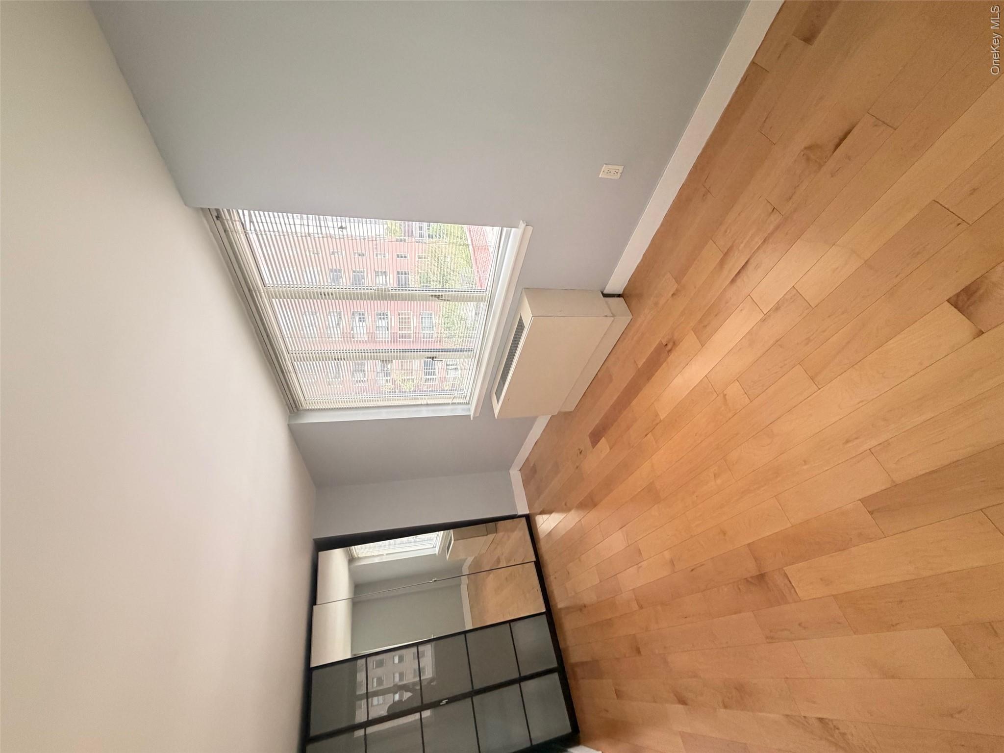 225 Rector Place, Unit 7E Manhattan, NY 10280 - Photo 5 of 19 Room featuring wood-finish flooring, a full-wall mirrored wardrobe with sliding panel doors, a large multi-pane window with blinds, and light-toned wall paint