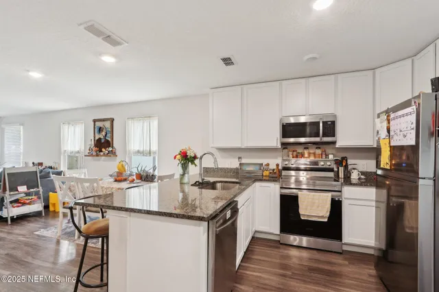 a kitchen with stainless steel appliances a sink a stove a refrigerator cabinets and a dining table