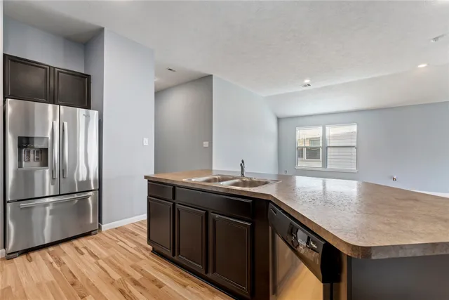 a kitchen with stainless steel appliances granite countertop a sink dishwasher a refrigerator and a stove with wooden floor