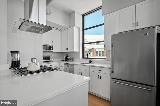 a kitchen with stainless steel appliances a sink dishwasher stove and white cabinets with wooden floor
