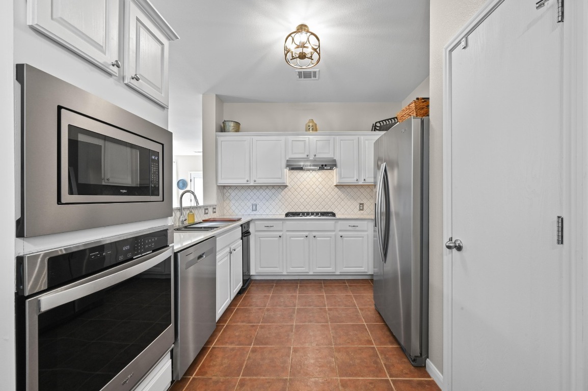 400 Tobin Drive Buda, TX 78610 - Photo 14 of 40 Kitchen with stainless steel appliances, white cabinets, light countertops, backsplash, and dark tile patterned flooring