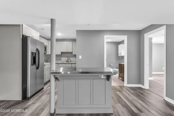 a kitchen with stainless steel appliances granite countertop a refrigerator a sink a stove and white cabinets with wooden floor