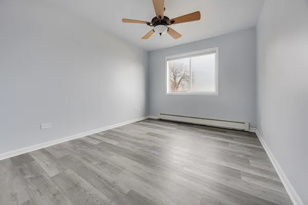 an empty room with wooden floor ceiling fan and windows