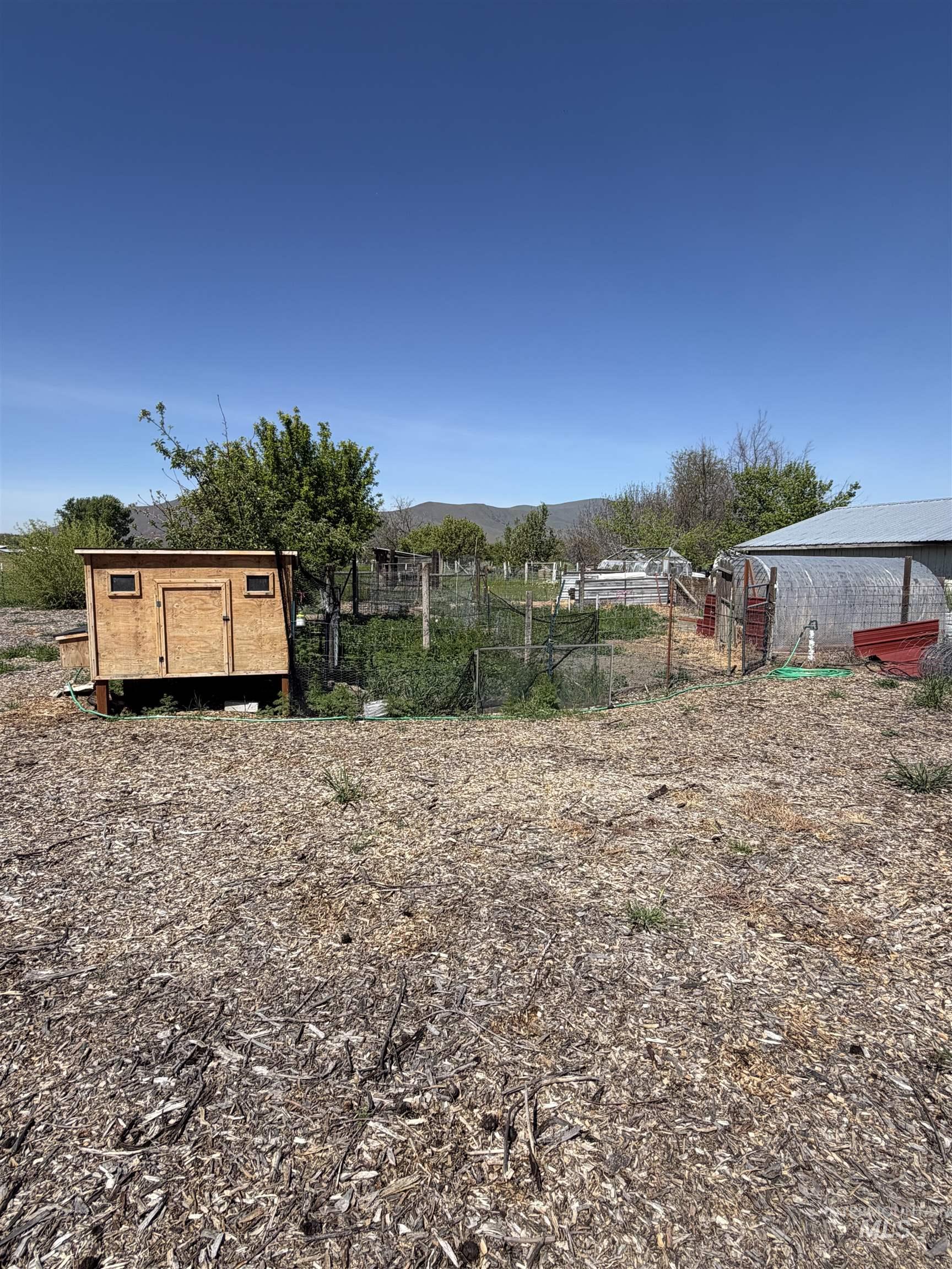 875 Eaton Road Weiser, ID 83672 - Photo 25 of 30 Expansive grounds featuring a woodchip-covered area, a fenced garden, a wood-sided utility shed, and a metal-roofed structure