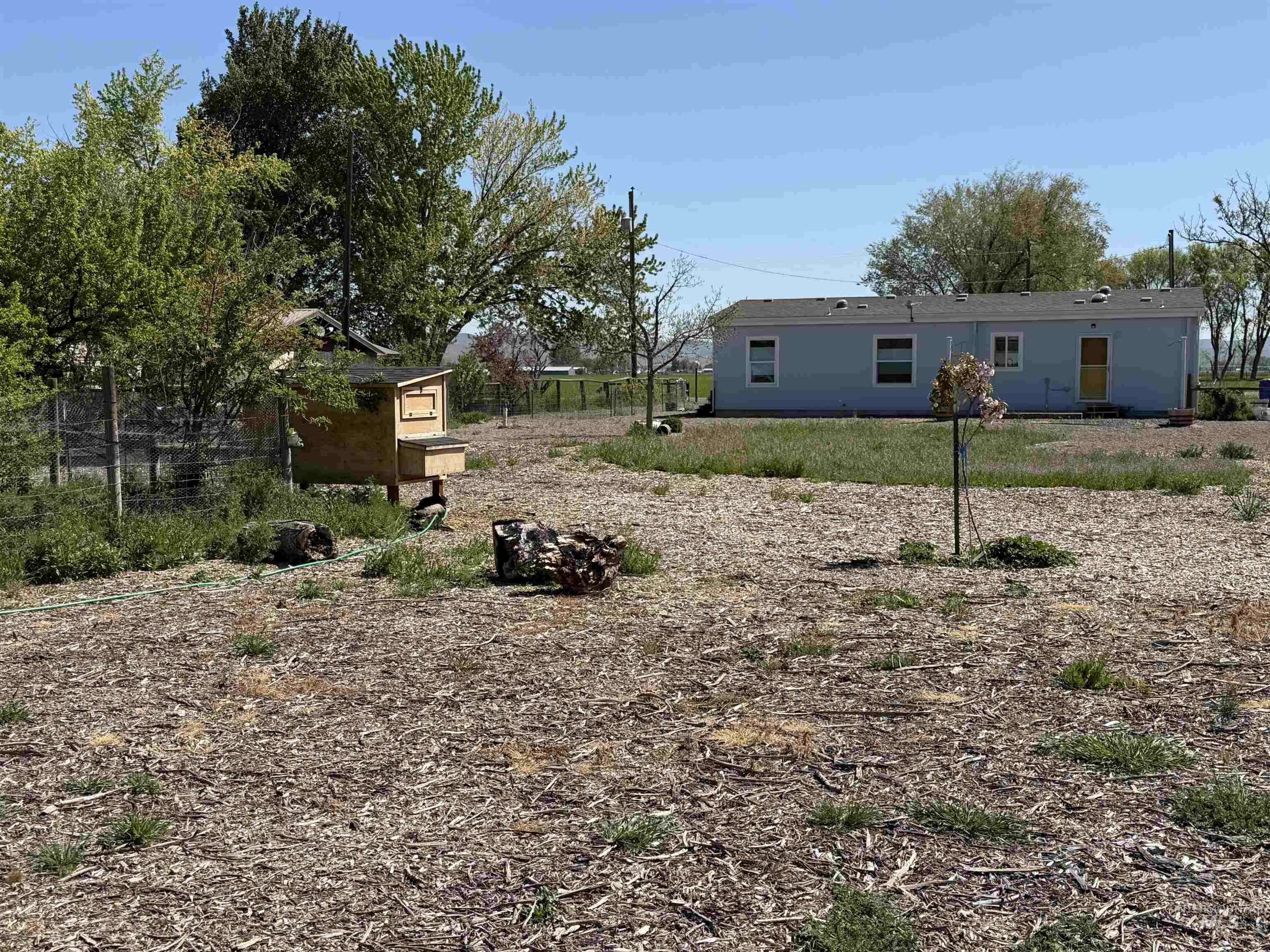875 Eaton Road Weiser, ID 83672 - Photo 27 of 30 Spacious exterior with wood chip ground cover, a light blue single-story residence, and an enclosed animal structure