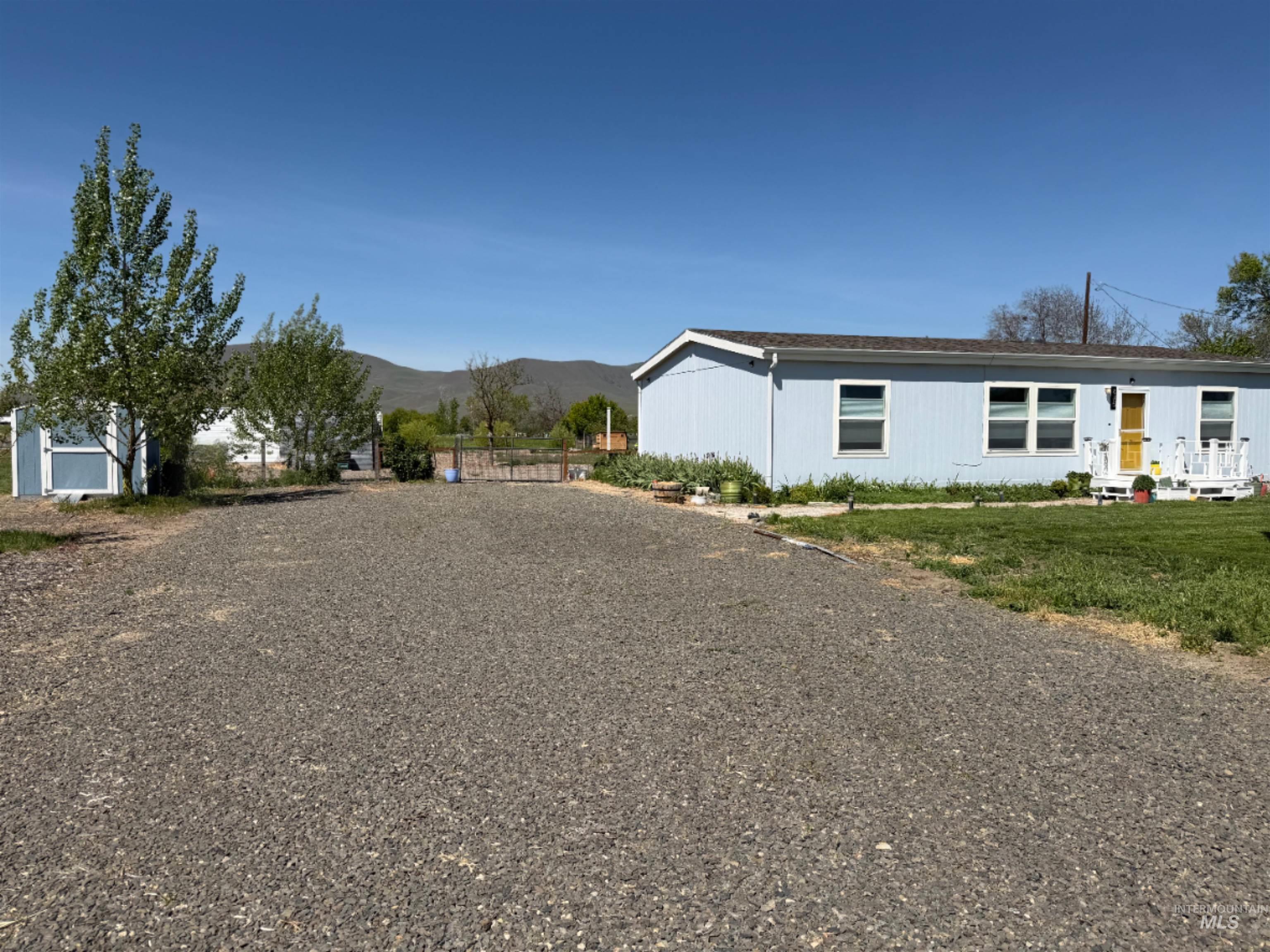 875 Eaton Road Weiser, ID 83672 - Photo 5 of 30 Spacious gravel lot with a light blue single-story residence featuring multiple windows and a yellow front door