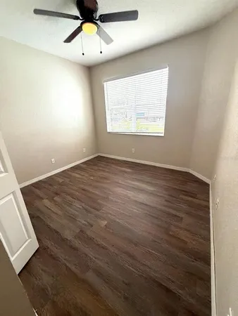 an empty room with wooden floor chandelier fan and windows