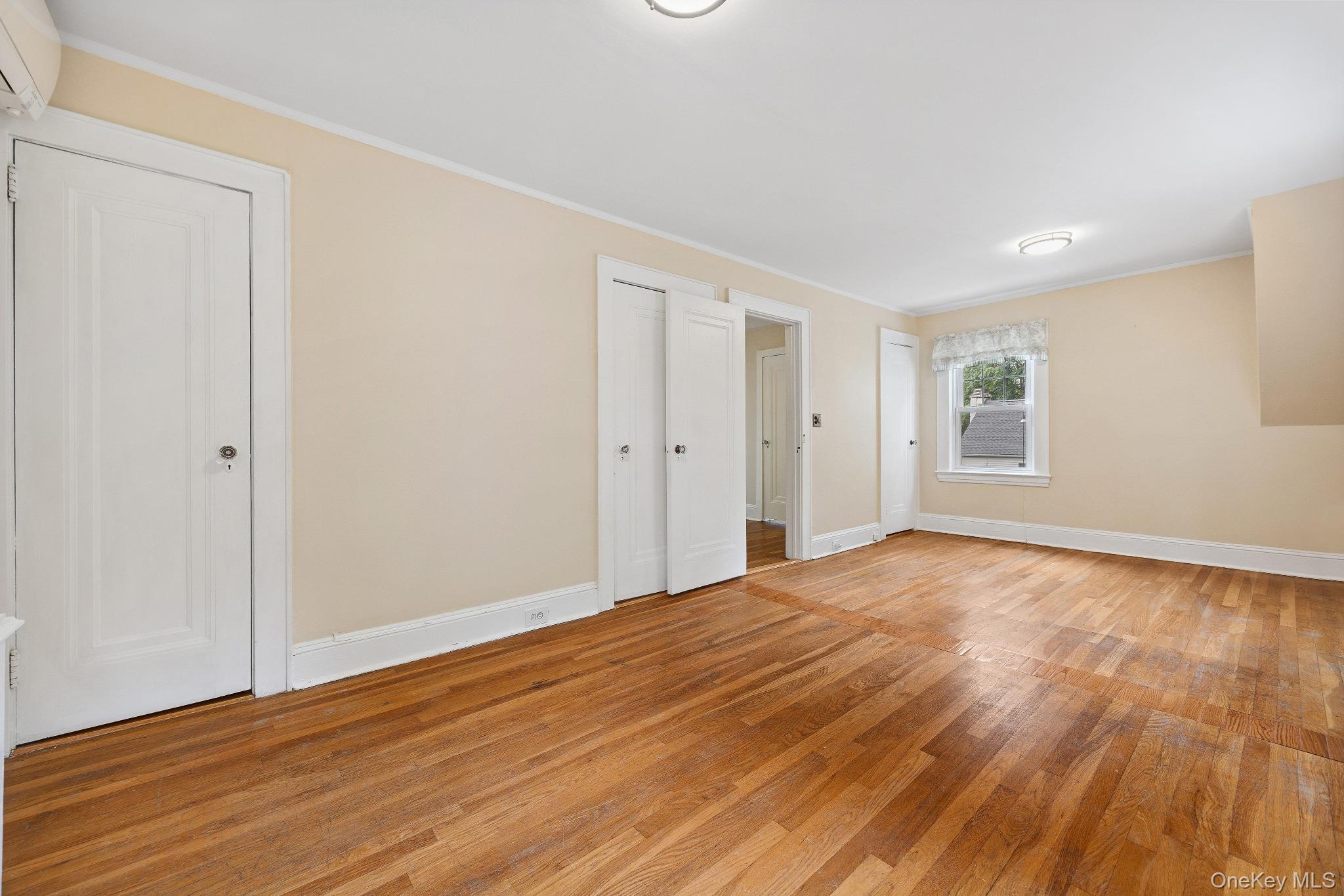 1235 Post Road Scarsdale, NY 10583 - Photo 18 of 30 Unfurnished bedroom with light wood-style flooring, ornamental molding, a wall unit AC, and two closets