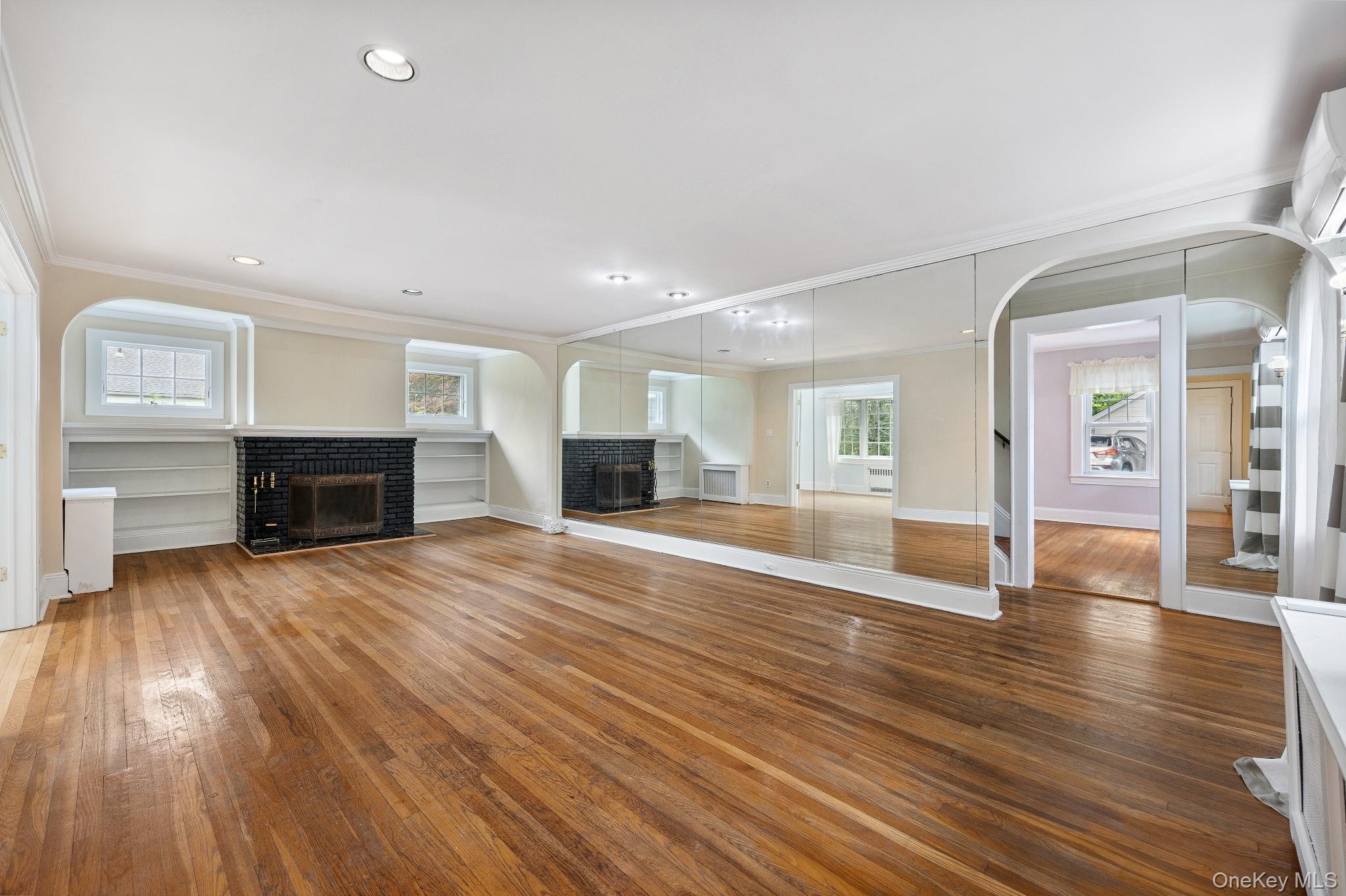 1235 Post Road Scarsdale, NY 10583 - Photo 5 of 30 Unfurnished living room featuring a brick fireplace, arched walkways, crown molding, wood-type flooring, and recessed lighting