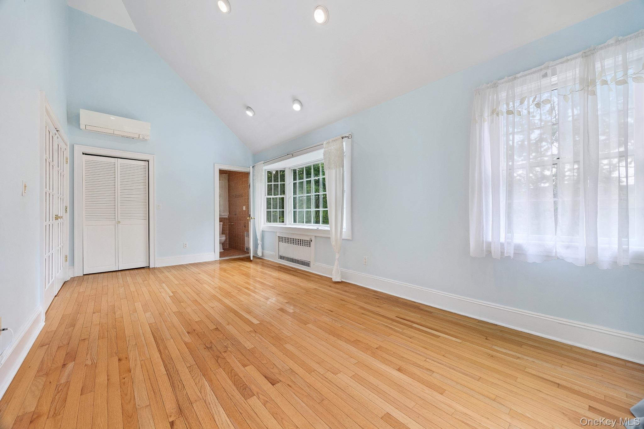 1235 Post Road Scarsdale, NY 10583 - Photo 8 of 30 Unfurnished bedroom featuring radiator heating unit, a wall mounted air conditioner, high vaulted ceiling, light wood-style floors, and a closet