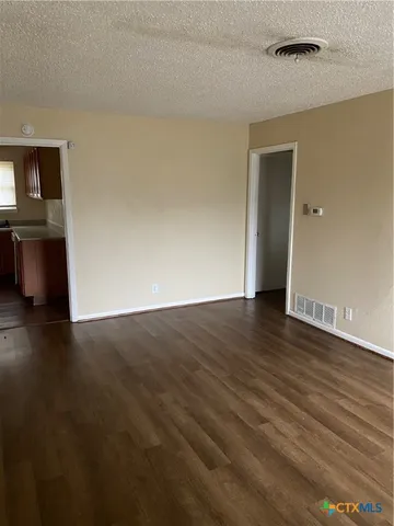 a view of an empty room with wooden floor and a ceiling fan