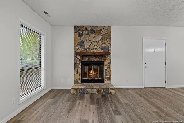 a view of an empty room with wooden floor fireplace and a window