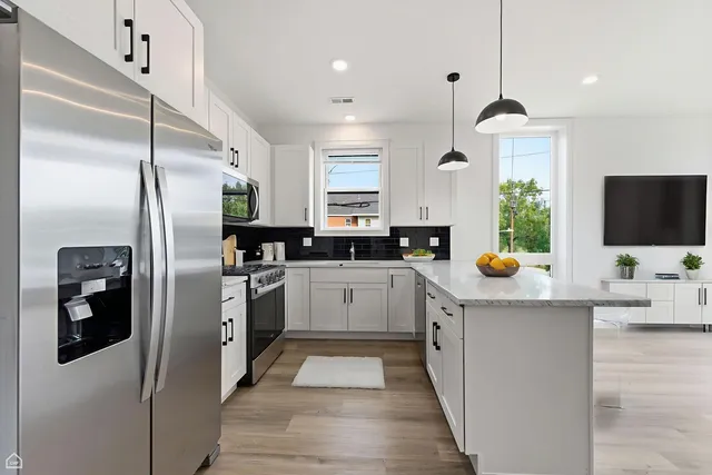 a kitchen with stainless steel appliances kitchen island granite countertop a refrigerator a sink a stove and chairs with wooden floor