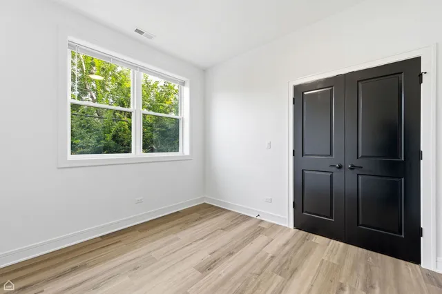 an empty room with wooden floor closet and windows
