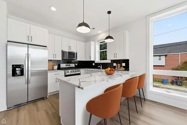 a kitchen with stainless steel appliances granite countertop a refrigerator a stove a sink a dining table and chairs with wooden floor