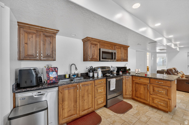 141 Wolverine Creek Elk Ridge, UT 84651 - Photo 25 of 47 Kitchen with a peninsula, stainless steel appliances, dark stone counters, wood finish cabinets, and a textured ceiling
