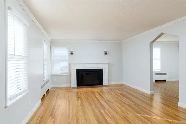 a view of an empty room with wooden floor fireplace and a window