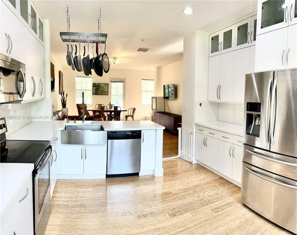 a kitchen with stainless steel appliances a stove a sink dishwasher a refrigerator and white cabinets with wooden floor