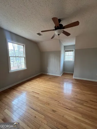 an empty room with wooden floor fan and windows