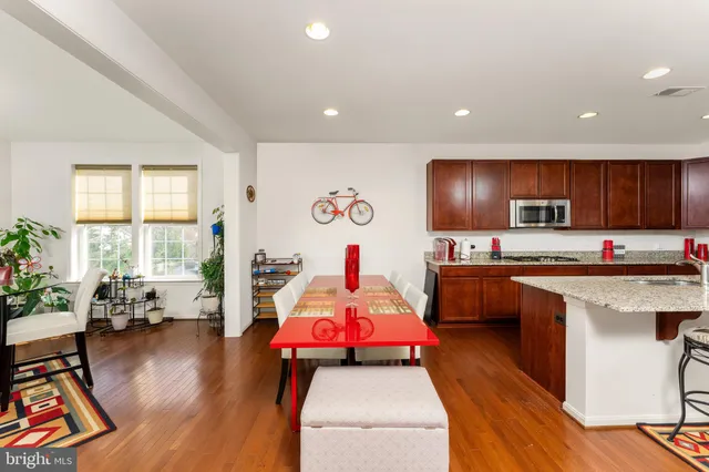 a kitchen with stainless steel appliances kitchen island granite countertop a stove top oven a sink dishwasher and a dining table with wooden floor