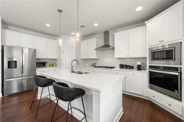 a kitchen with stainless steel appliances granite countertop a sink a stove a refrigerator and island with wooden floor