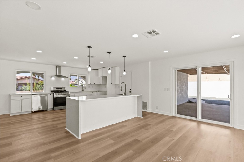 2852 East San Angelo Road Palm Springs, CA 92262 - Photo 6 of 25 a large kitchen with kitchen island a stove a refrigerator a sink dishwasher with a dining table and chairs with wooden floor