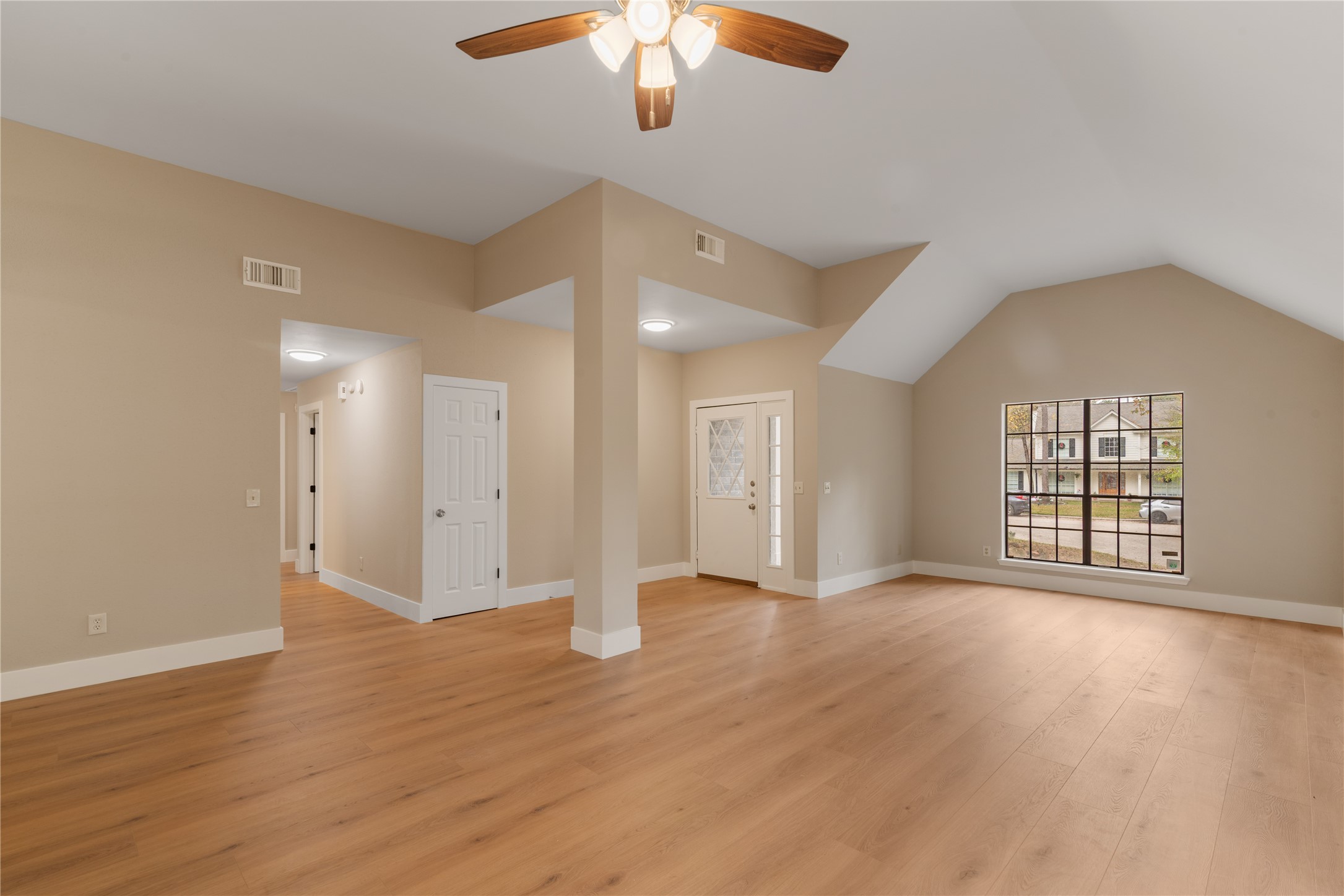10 White Fawn Drive Spring, TX 77381 - Photo 5 of 25 This spacious living area features vaulted ceilings, warm wood flooring, and a ceiling fan for comfort. A large window provides ample natural light and a view of the neighborhood. The neutral walls offer a versatile backdrop, and there's convenient access to other rooms and the front door.