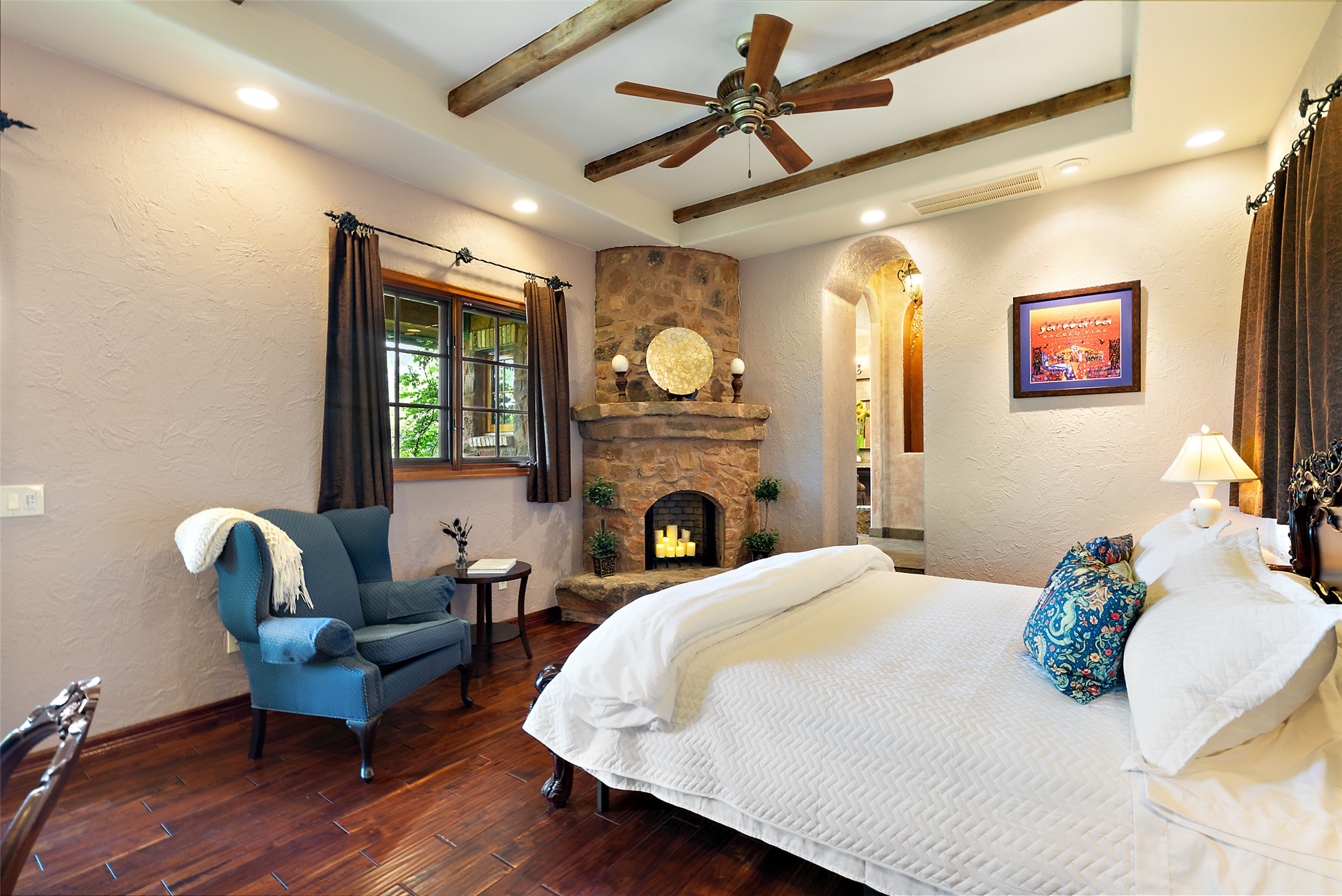 1354 The High Road Austin, TX 78746 - Photo 23 of 40 A spacious primary bedroom features rich hardwood flooring, a stone fireplace, and rustic exposed beams across the ceiling.