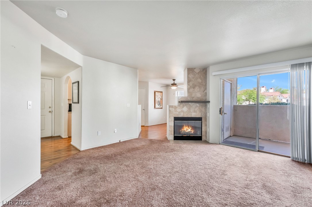 698 South Racetrack Road, Unit 1512 Henderson, NV 89015 - Photo 7 of 30 A stone-faced fireplace and sliding glass doors anchoring an open-concept living area with carpet flooring.